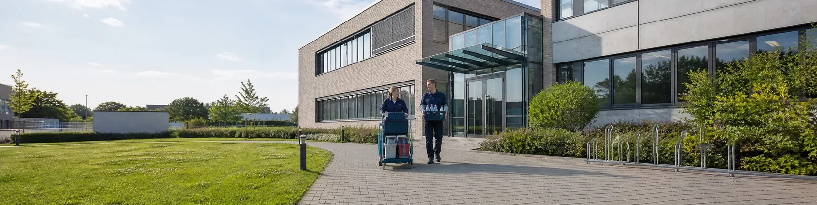 Reinigungsteam mit Reinigungswagen auf dem Weg zum Eingang eines Verwaltungsgebäudes